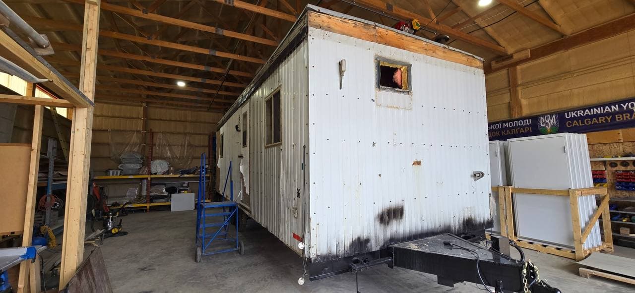 An older office trailer with worn siding and an open window opening in the Excel Trailers workshop