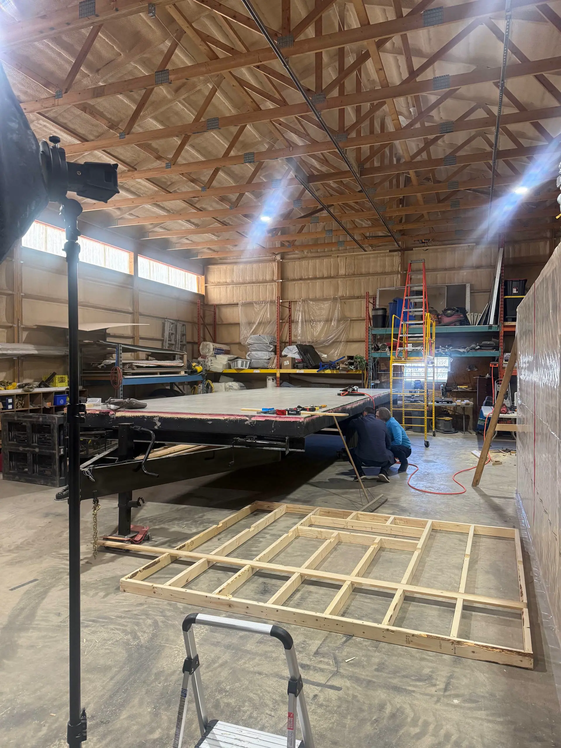 Sealed office trailer floor deck on the chassis with the first wall frame laid out flat on the shop floor