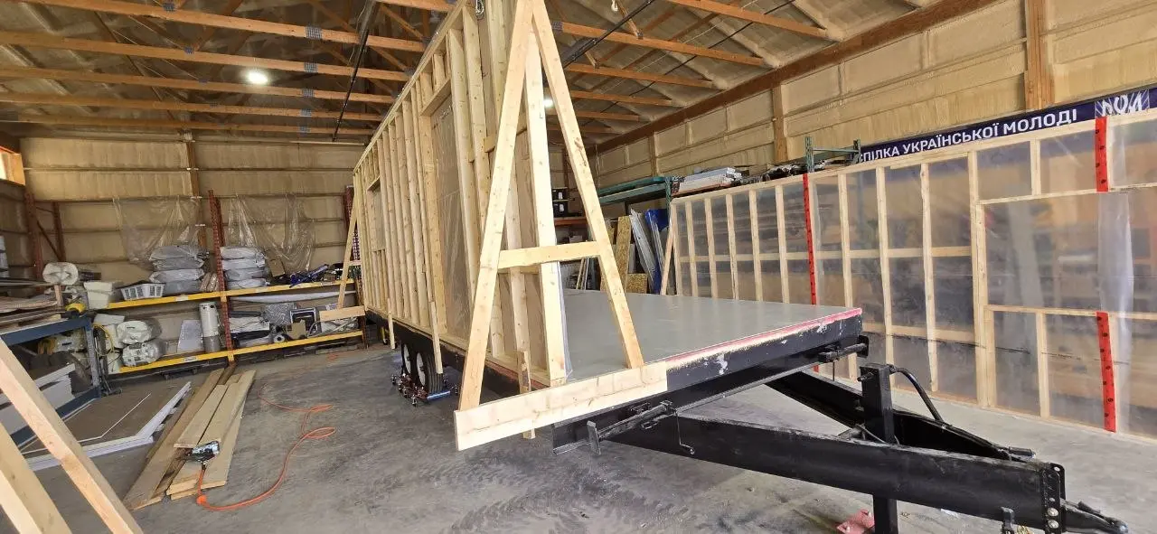 Office trailer walls standing on the trailer deck, braced with timber A-frames inside the shop