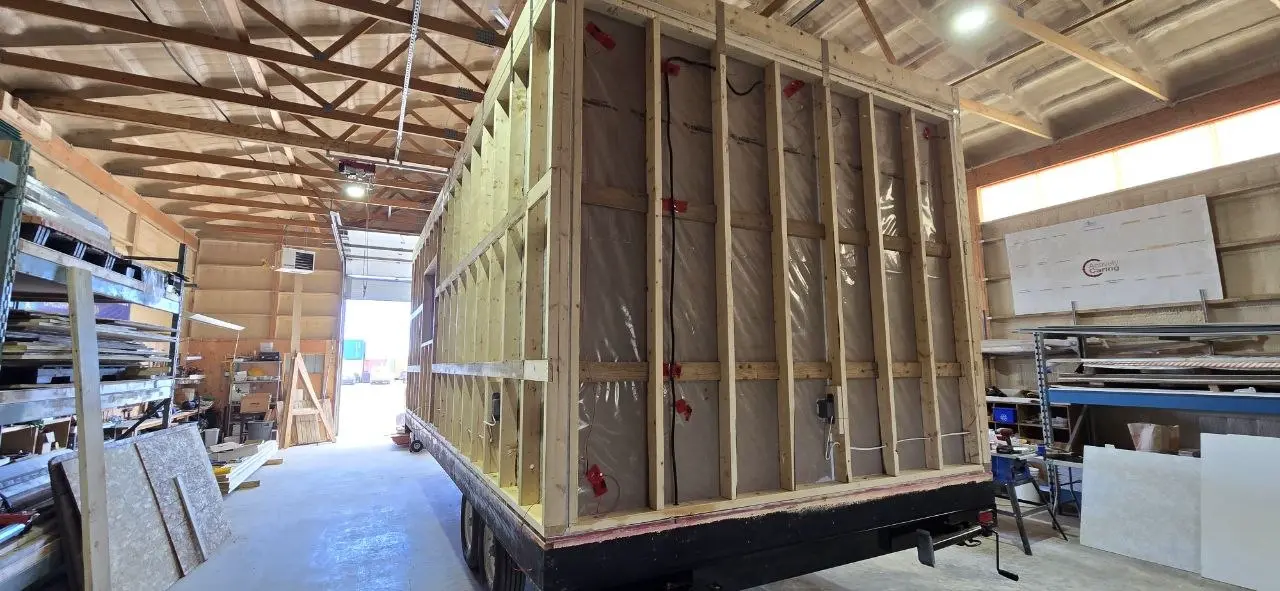Electrical rough-in inside a new office trailer, with boxes and wiring runs visible over the vapour barrier