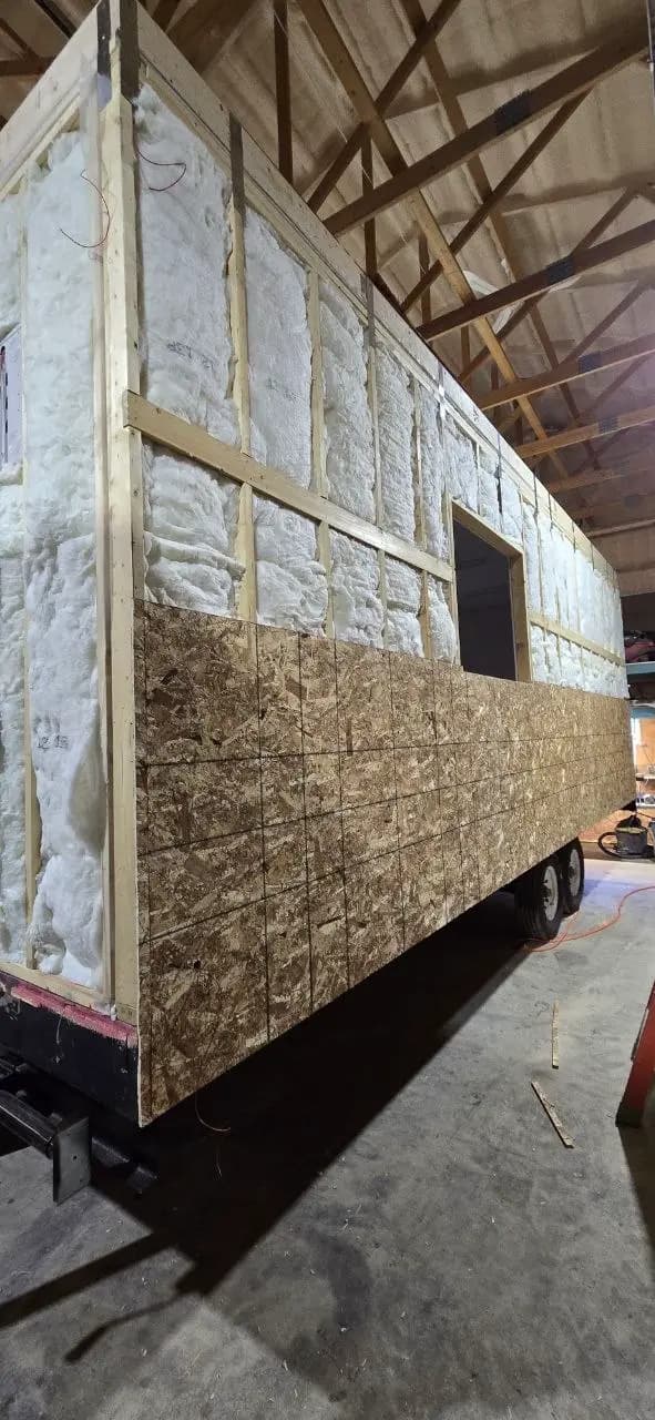 Batt insulation filling the wall cavities of a new office trailer with exterior sheathing going on